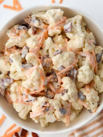 A bowl of cauliflower salad dotted with cheese and bacon.