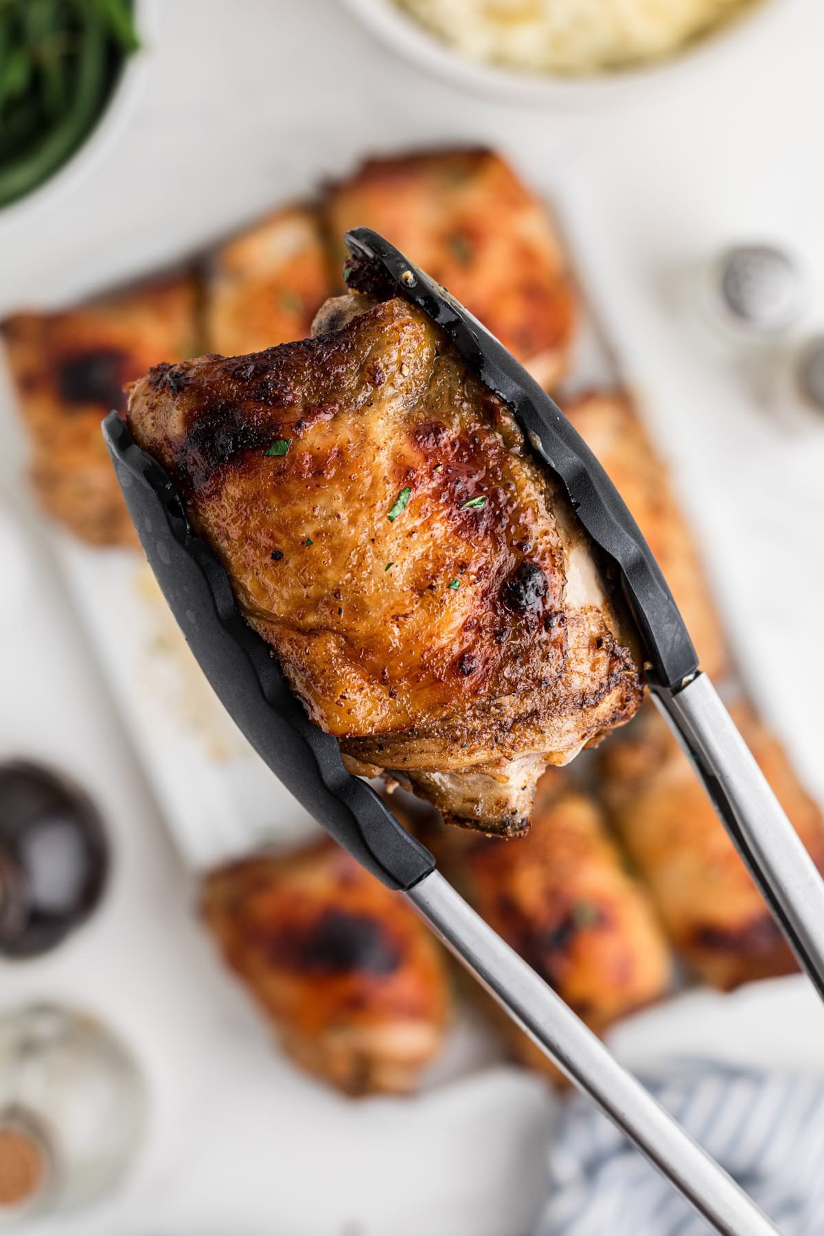 A pair of tongs lifting up a baked chicken thigh.