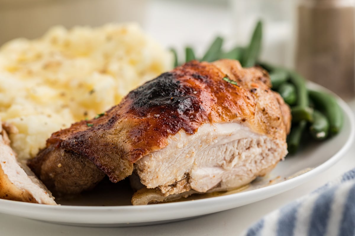 A close up of a chicken thigh served with mashed potato and green beans.