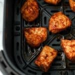 An air fryer basket with several unbreaded chicken bites.