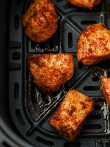 An air fryer basket with several unbreaded chicken bites.