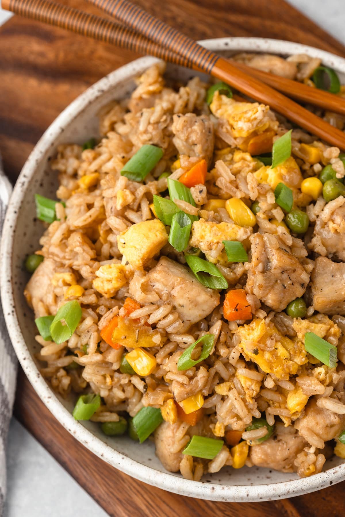 A bowl of chicken fried rice with a pair of chopsticks on the side of the bowl.