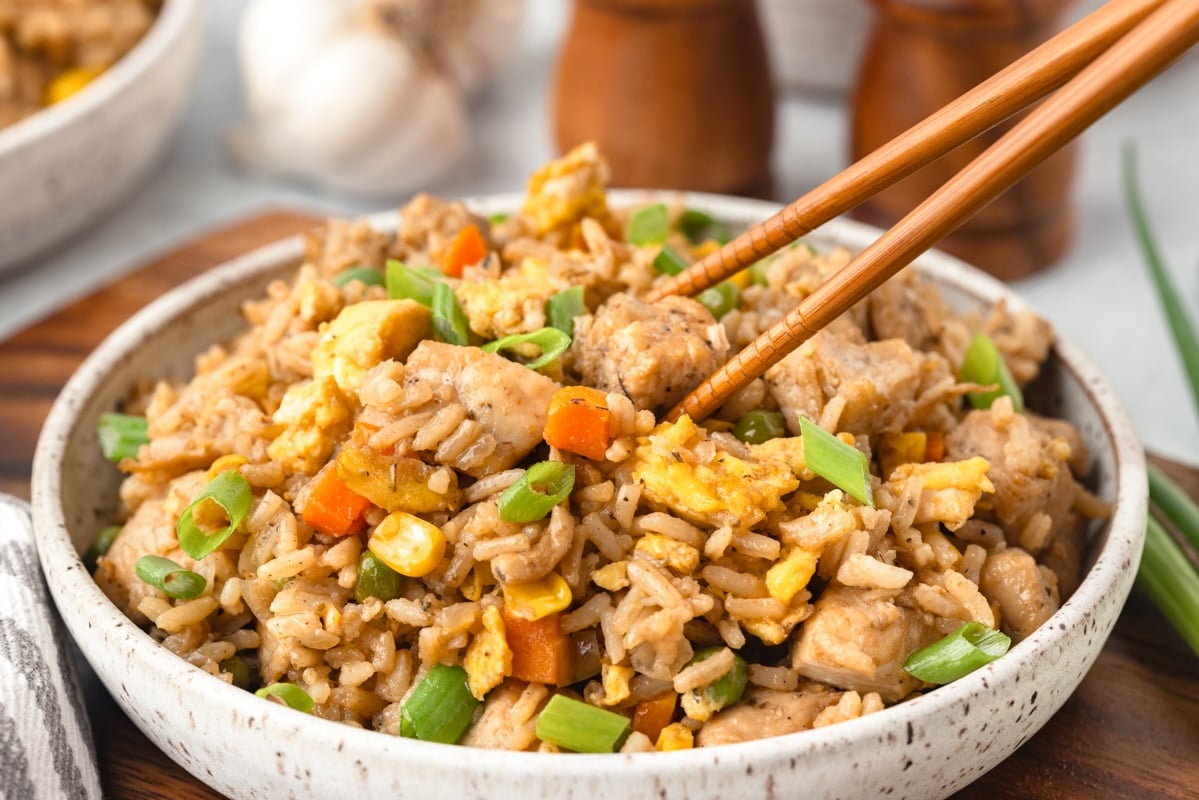 A bowl of chicken fried rice with chopsticks taking a portion.