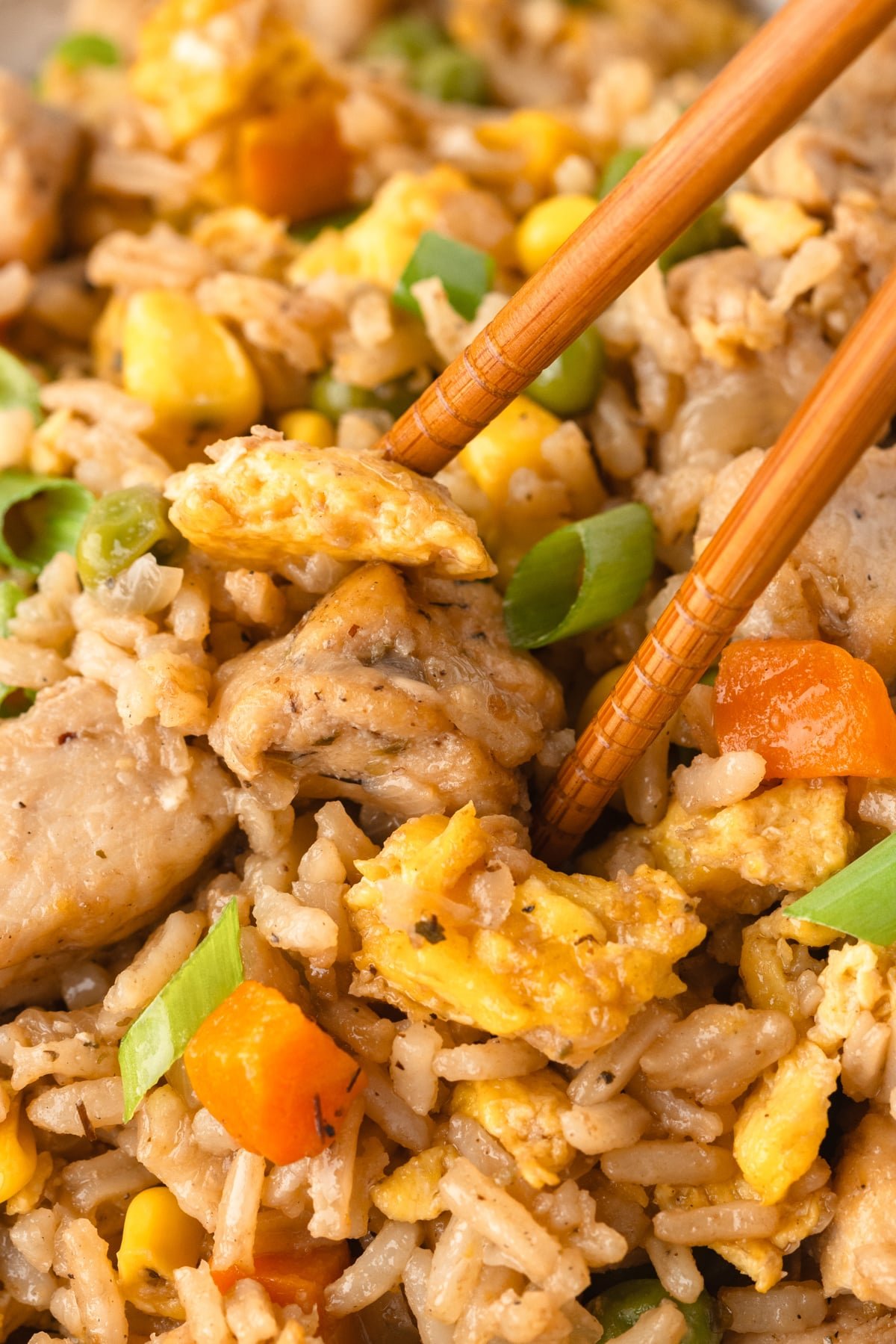 A pair of chopsticks taking a portion of chicken fried rice.