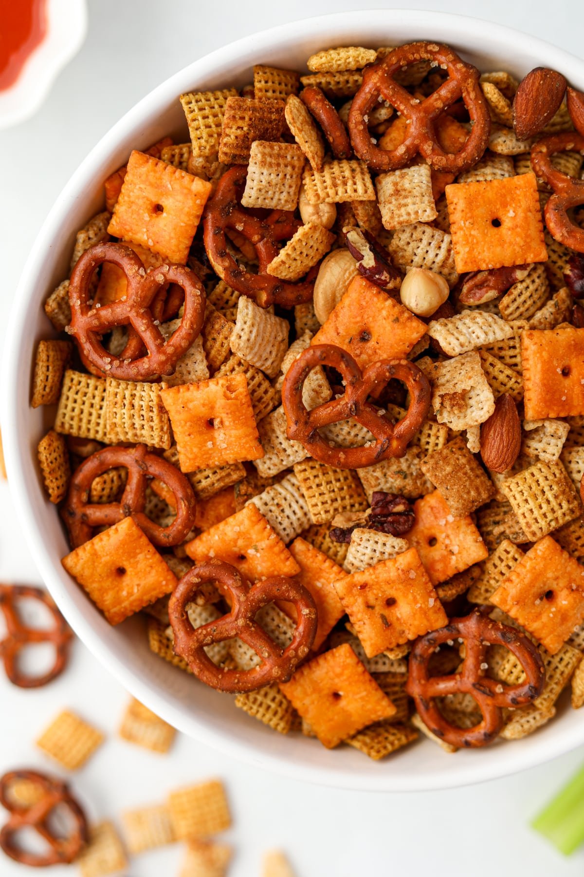 A white bowl filled with snack mix featuring pretzels, chex cereal, nuts, and cheez-its. 