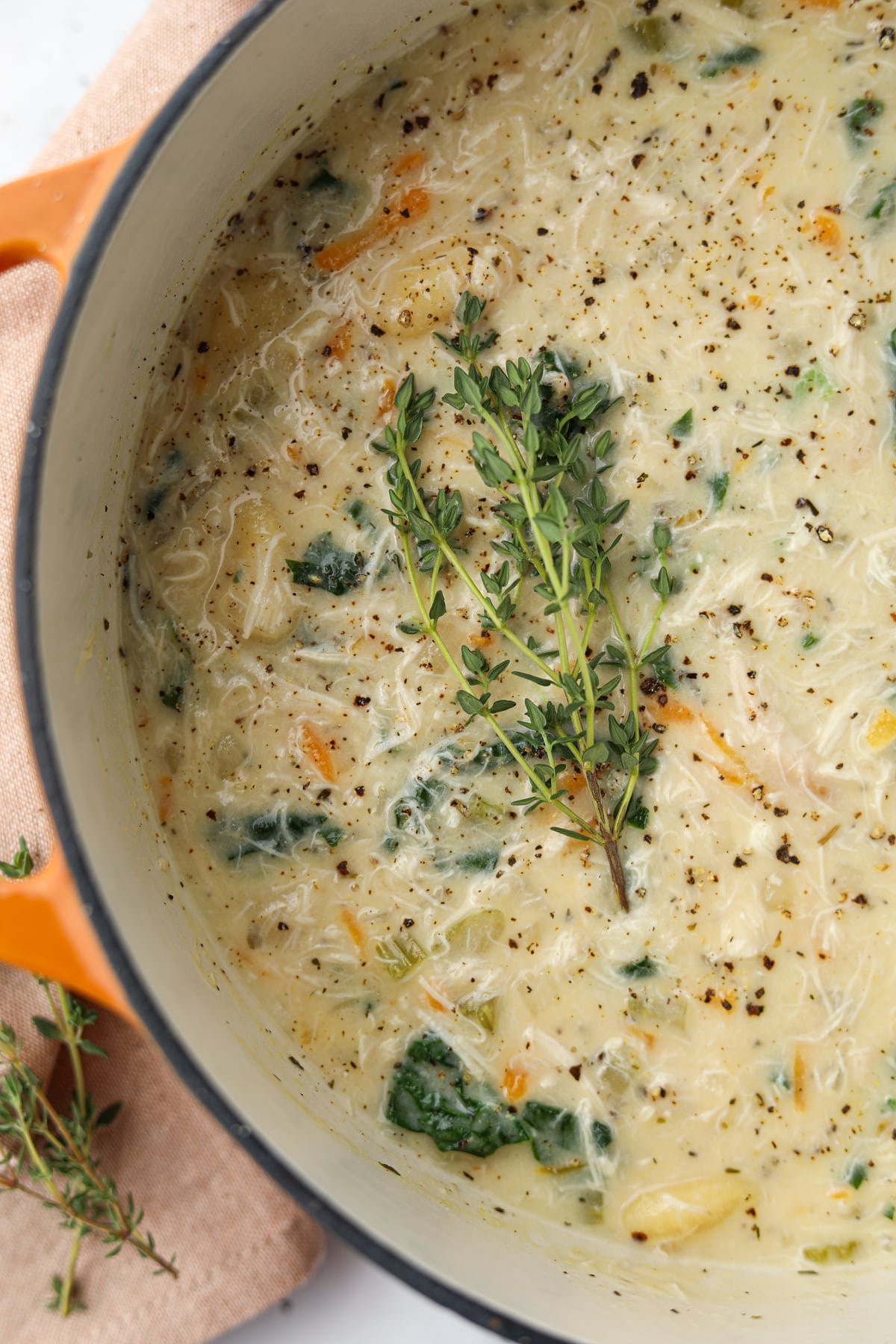 A dutch oven with a creamy soup inside, garnished with fresh thyme twigs.