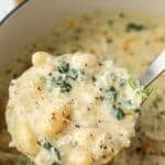 A ladle of creamy chicken soup with gnocchi being lifted from a pot.