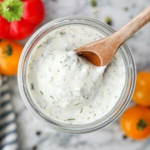 Scooping ranch dressing from a glass jar with a wooden spoon.