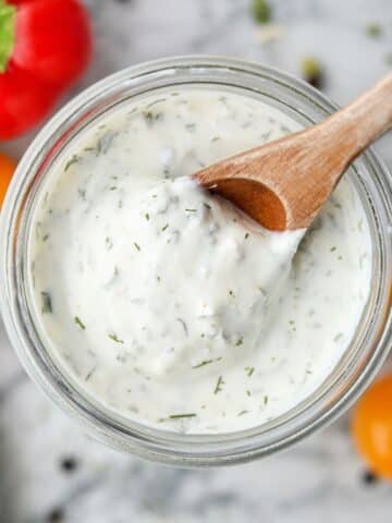 Scooping ranch dressing from a glass jar with a wooden spoon.