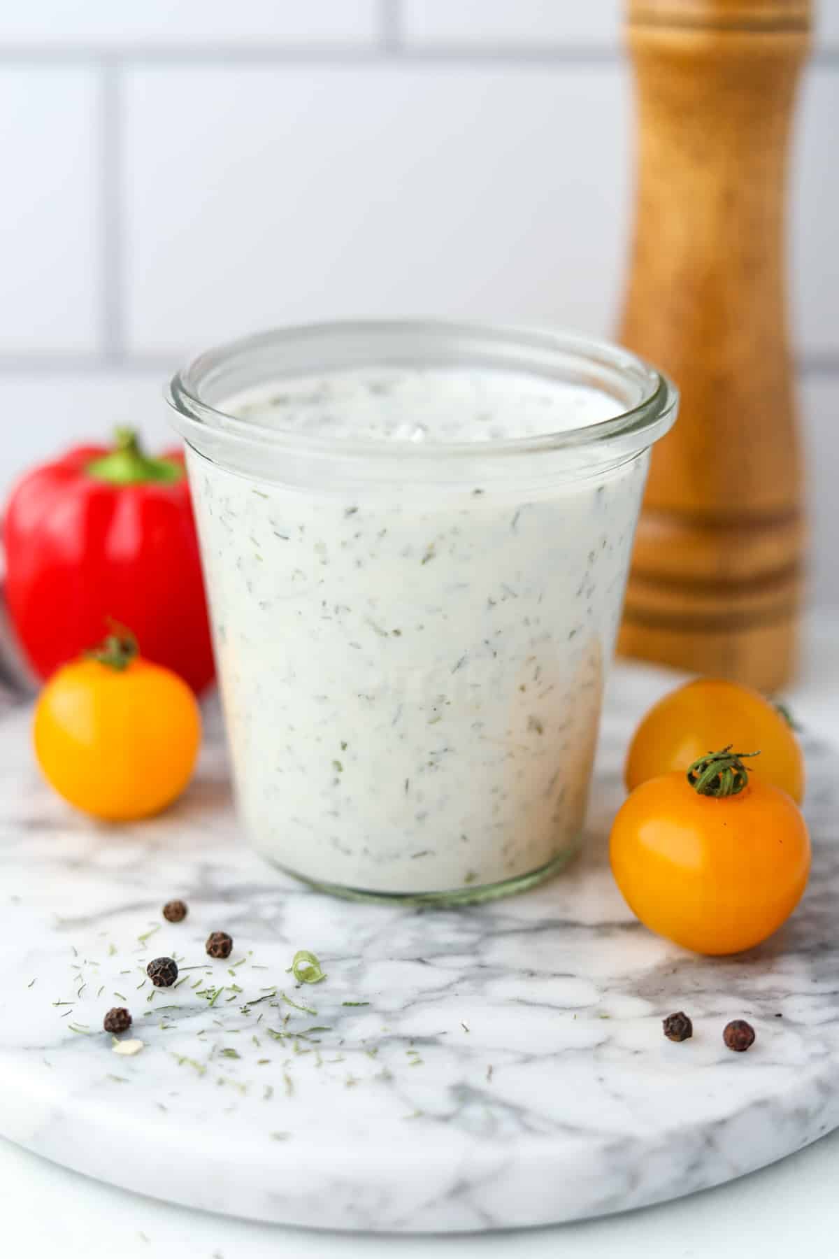 A glass jar filled with homemade ranch dressing, with veggies in the background.