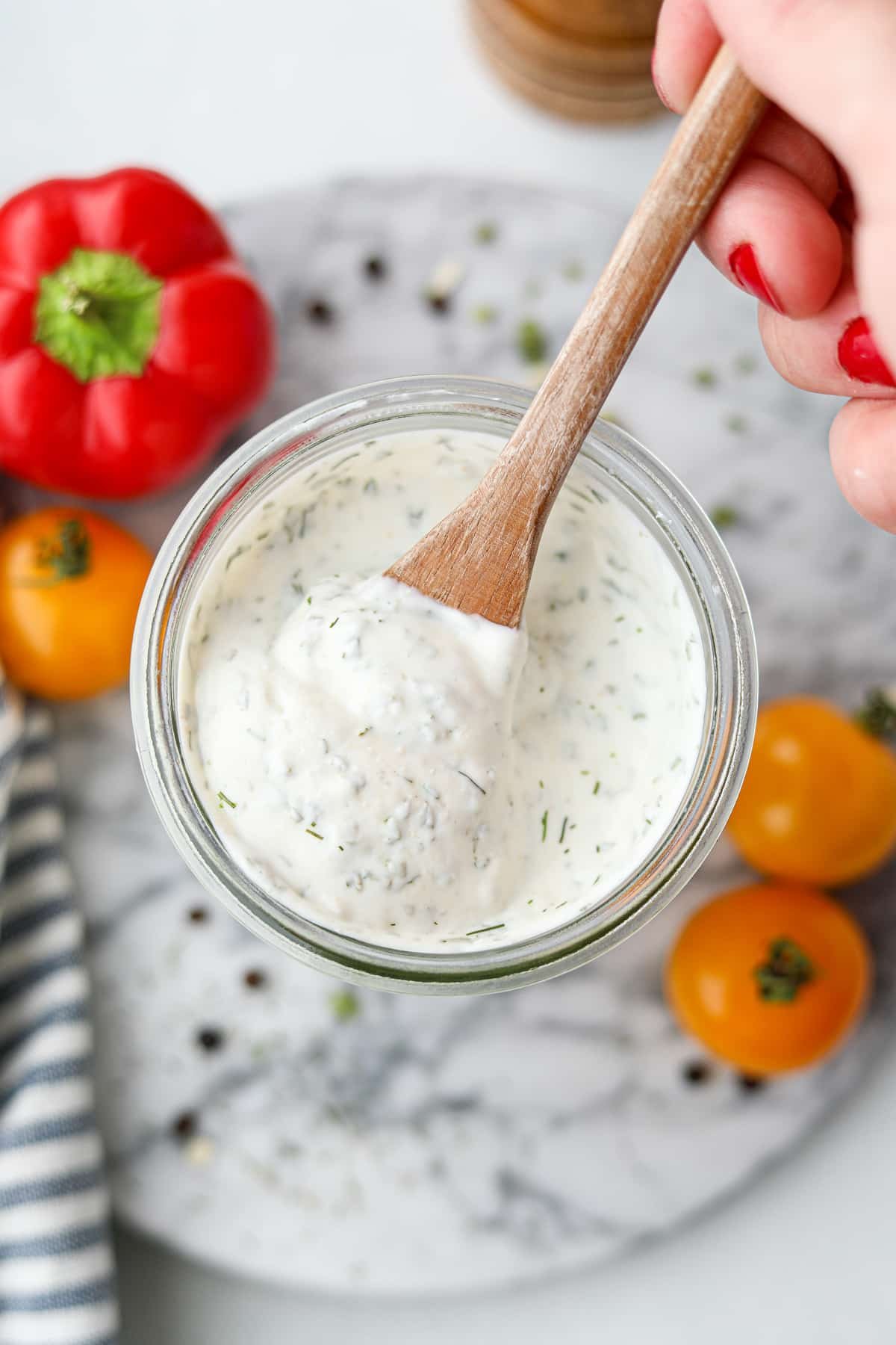 Scooping ranch dressing from a jar with a small wooden spoon.