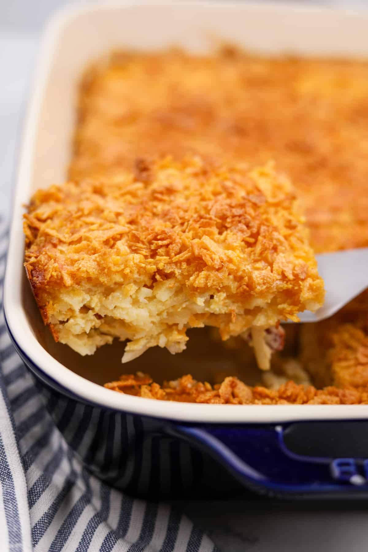 Lifting a portion of hash brown casserole from a baking dish.