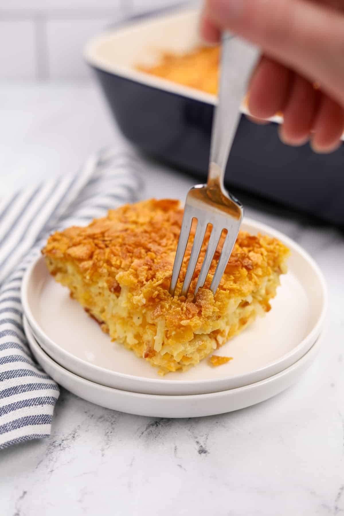 A fork taking a small portion of breakfast casserole from a plate.