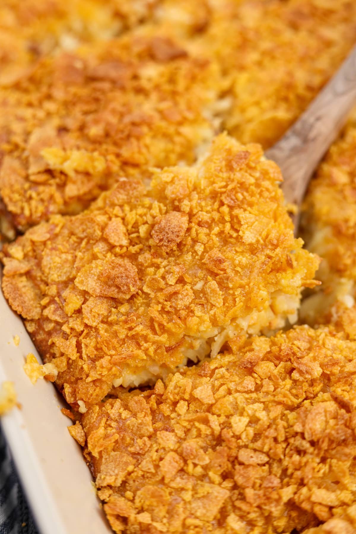 A wooden spatula serving up a square of breakfast casserole topped with crunchy cornflakes. 