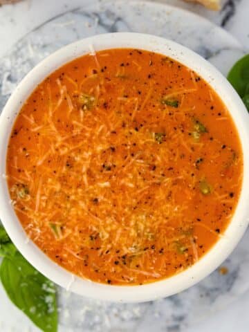 A bowl of cherry tomato soup garnished with parmesan cheese, basil, and cracked black pepper.