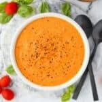 A bowl of cream tomato soup with cherry tomatoes and basil around the outside.