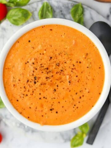 A bowl of cream tomato soup with cherry tomatoes and basil around the outside.