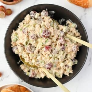 A black bowl filled with creamy chicken salad dotted with grapes.