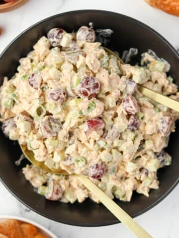 A black bowl filled with creamy chicken salad dotted with grapes.