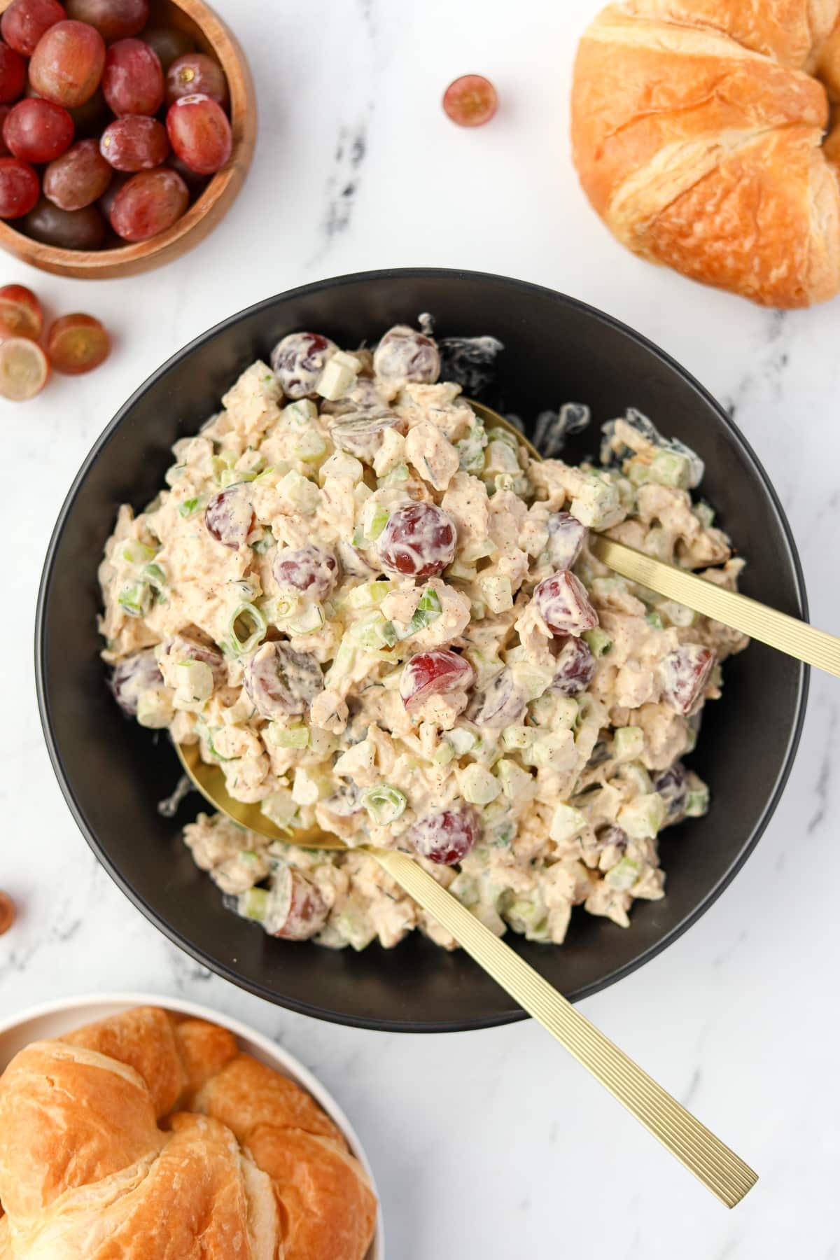 A bowl of chicken salad being tossed with serving spoons.