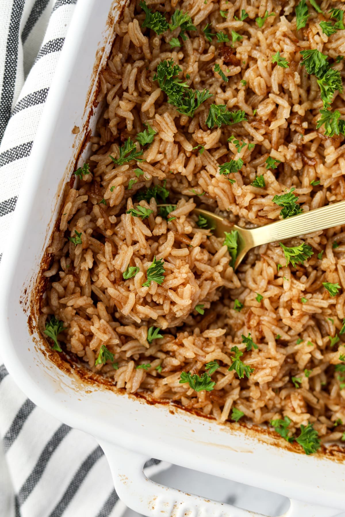 A white baking dish filled with baked rice garnished with parsley.