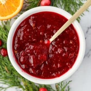 A small bowl of cranberry sauce being stirred with a gold spoon.