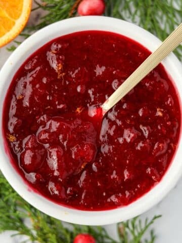 A small bowl of cranberry sauce being stirred with a gold spoon.