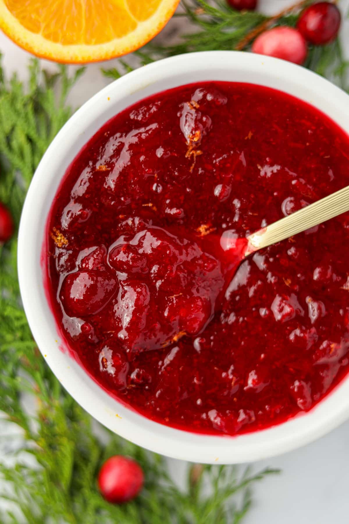 A small bowl filled with cranberry sauce, and a gold spoon stirs the contents.