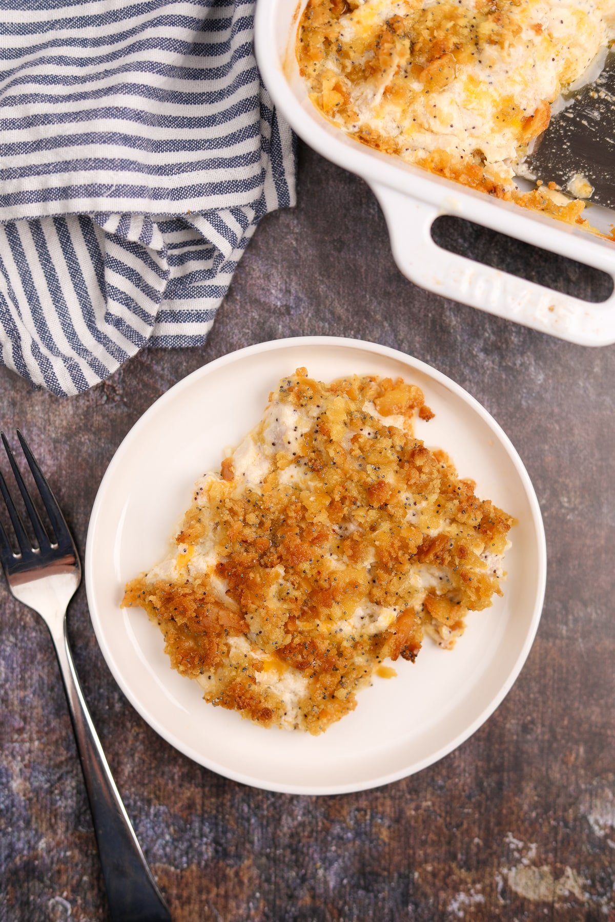 A portion of poppy seed chicken on a white plate, with a casserole dish beside it.