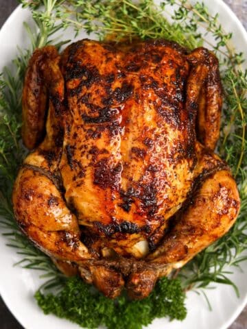 A whole roasted chicken on a white platter, garnished with fresh herbs.