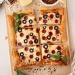 A square puff pastry pizza topped with pepperoni, olives, and fresh basil.