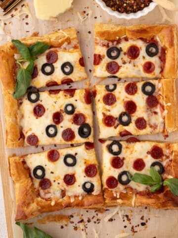 A square puff pastry pizza topped with pepperoni, olives, and fresh basil.