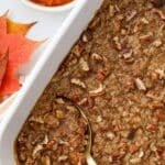 A gold serving spoon taking a portion of pumpkin casserole topped with pecans.