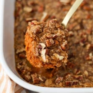 A spoon taking a portion of pumpkin casserole topped with pecans.