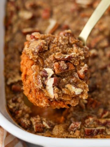 A spoon taking a portion of pumpkin casserole topped with pecans.