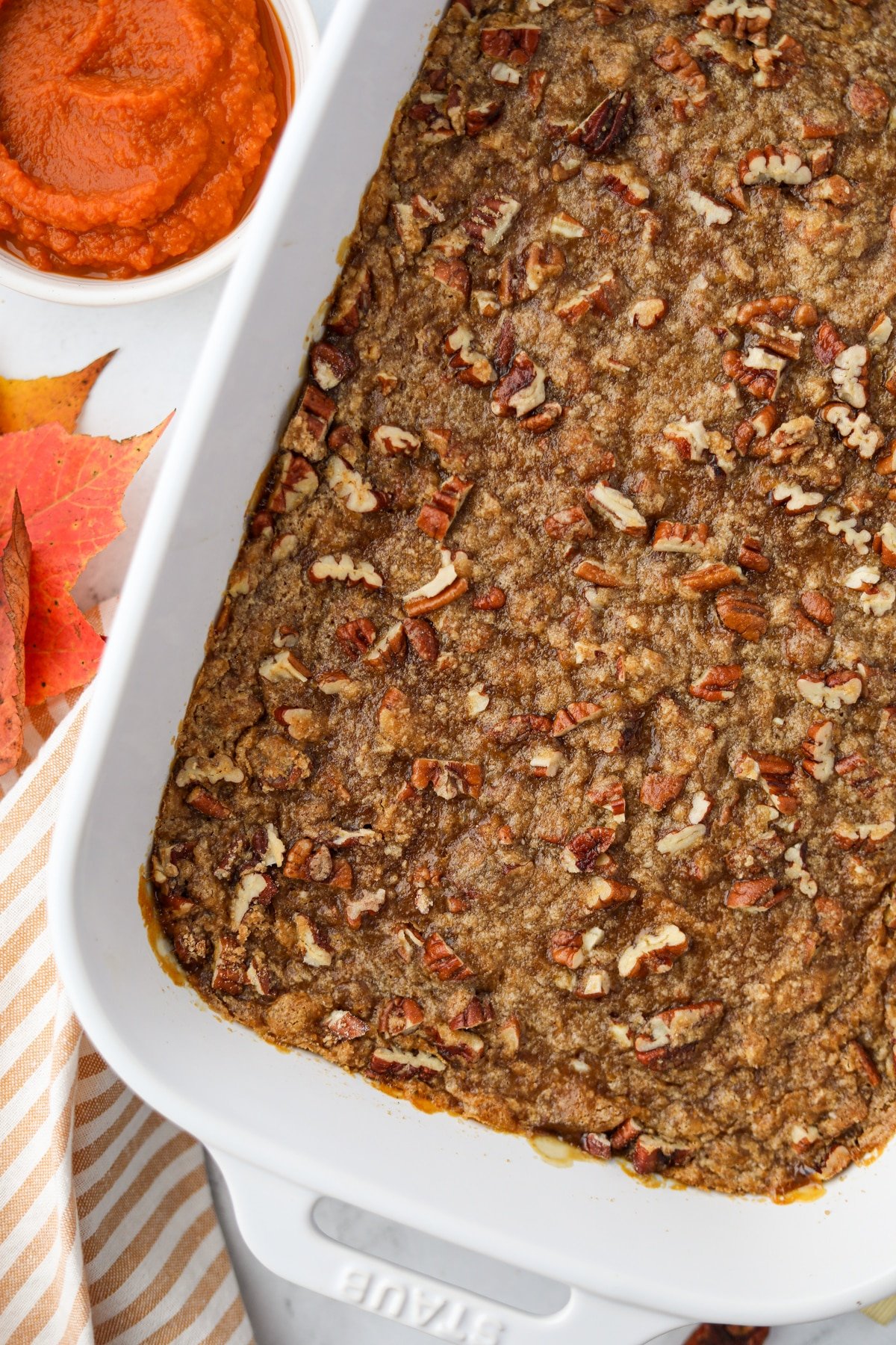 A white baking dish filled with a casserole topped with pecans and brown sugar.