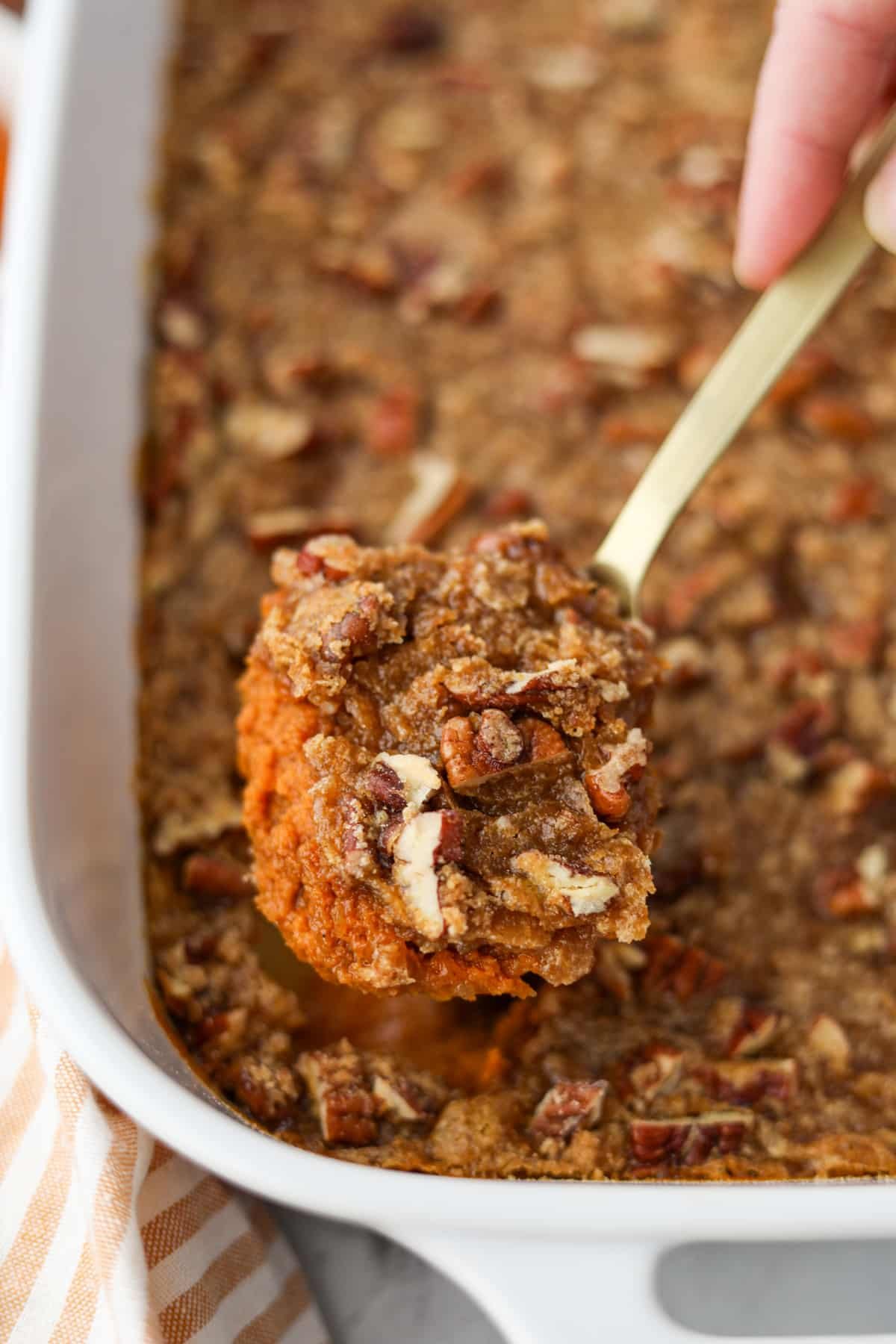 Scooping a portion of pumpkin casserole topped with pecans.