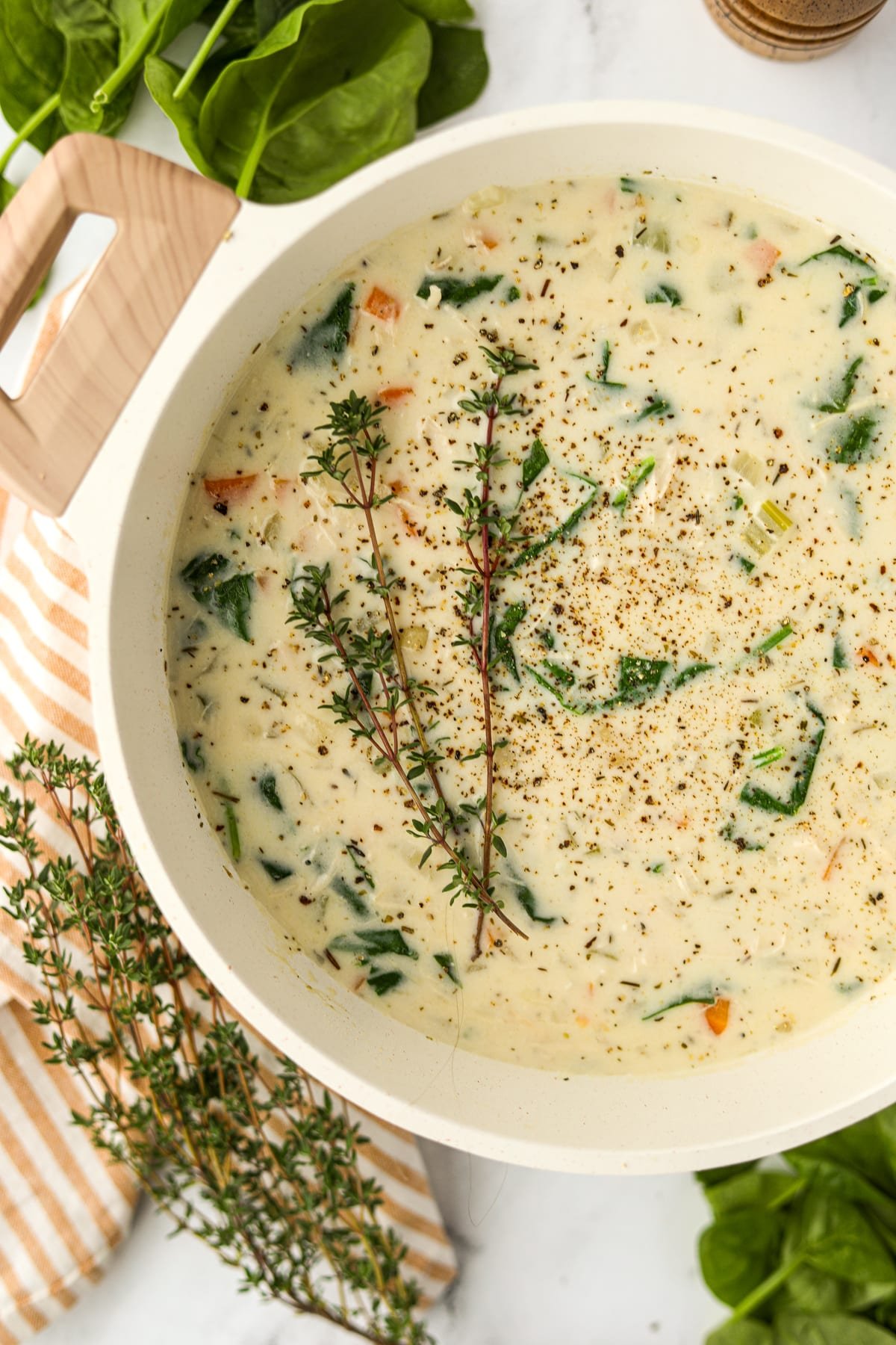 A pot of cream soup garnished with fresh thyme sprigs.