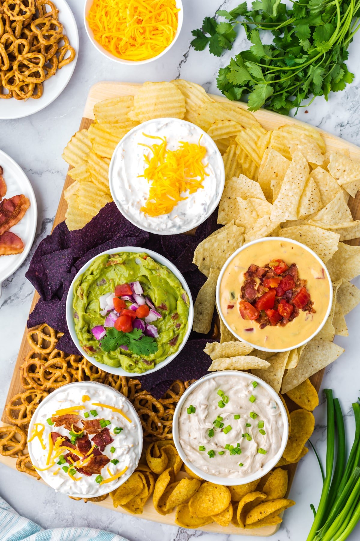 A board with five different dips with various chips arranged on a board below.