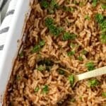 A white baking dish filled with cooked rice, being scooped with a serving spoon.