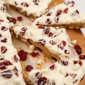 A triangular cranberry bliss bar topped with dried cranberries and cream cheese frosting.