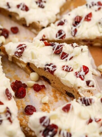 A triangular cranberry bliss bar topped with dried cranberries and cream cheese frosting.