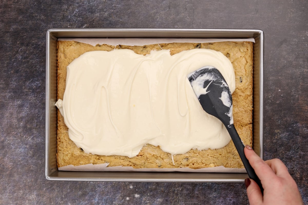 Spreading cream cheese frosting over a chilled blondie base layer.