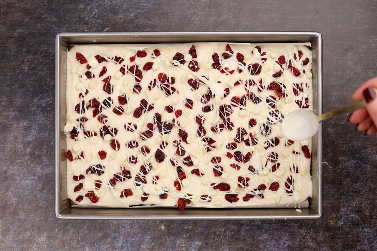 Drizzling white chocolate over cream cheese frosting and dried cranberries.