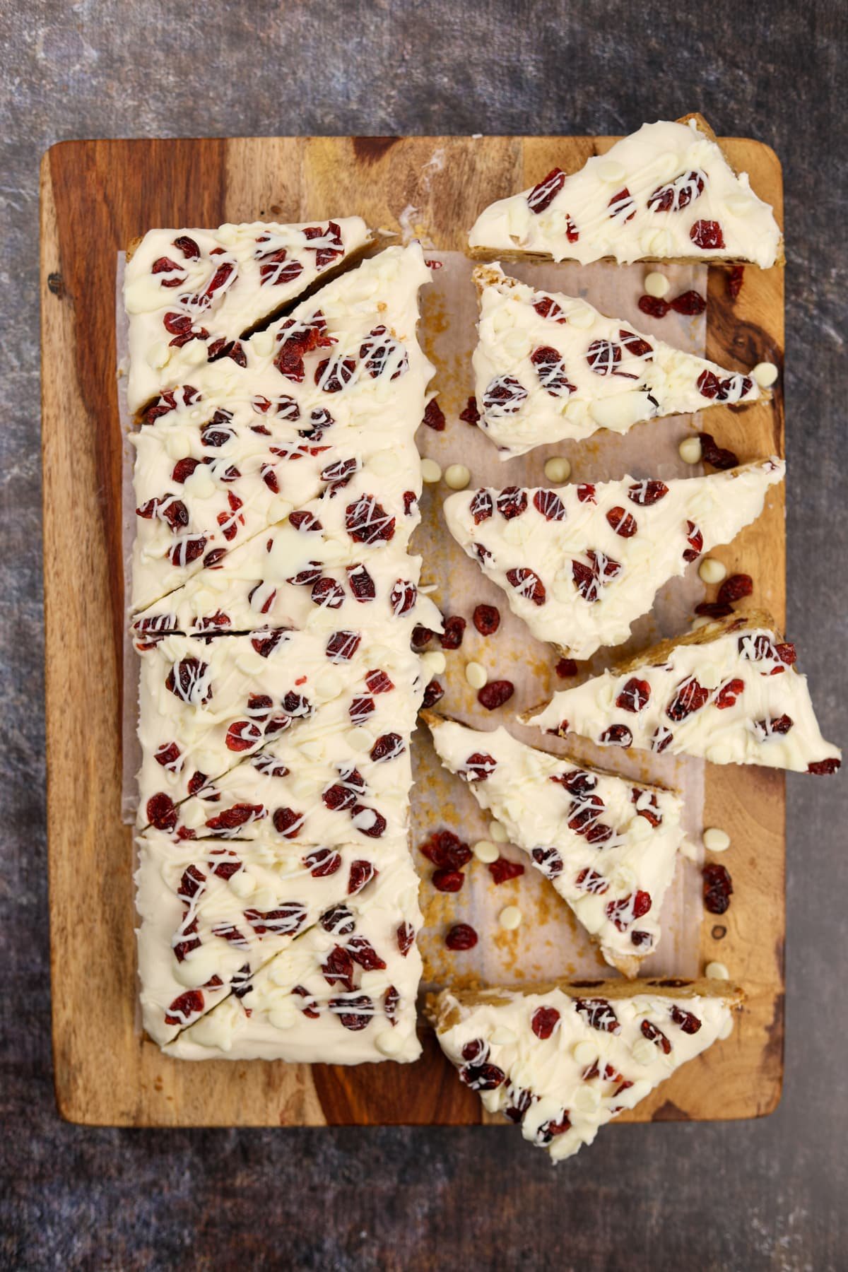 Slicing frosted blondies into triangles on a wooden cutting board.