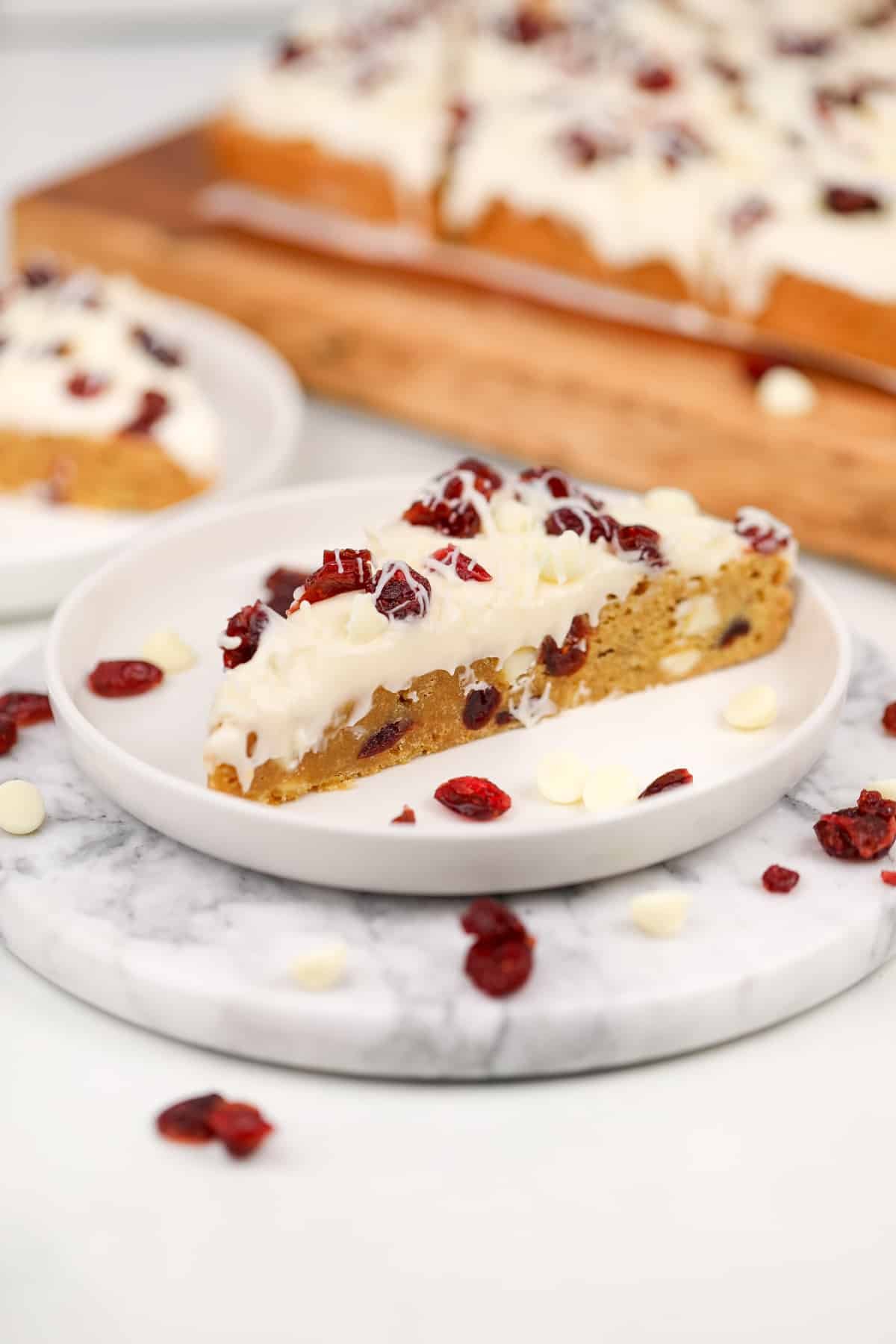 A triangular blondie bar topped with cream cheese frosting and dried cranberries.