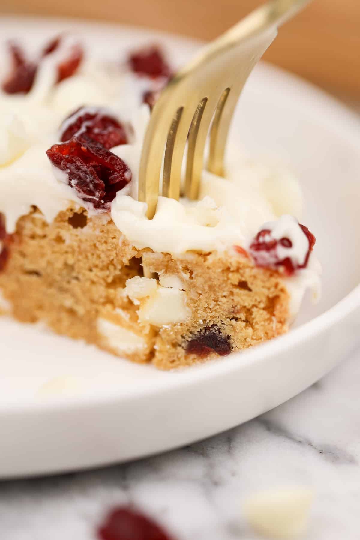 A fork sinking into a soft blondie layer that's topped with cream cheese frosting.