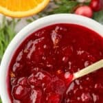 A small bowl of cranberry sauce, with a sliced orange in the background.