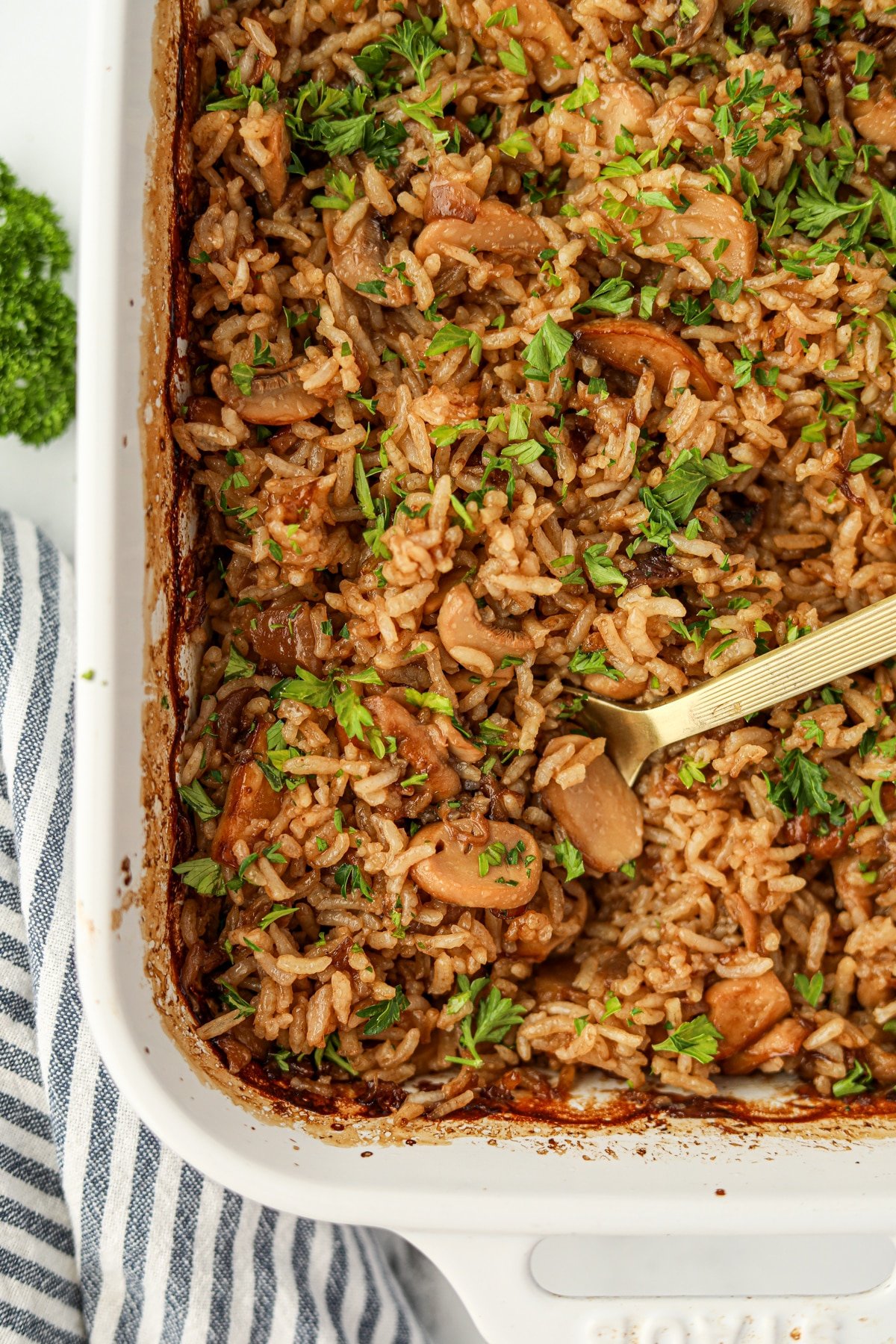 A spoon resting in a baking dish filled with a mushroom rice casserole.