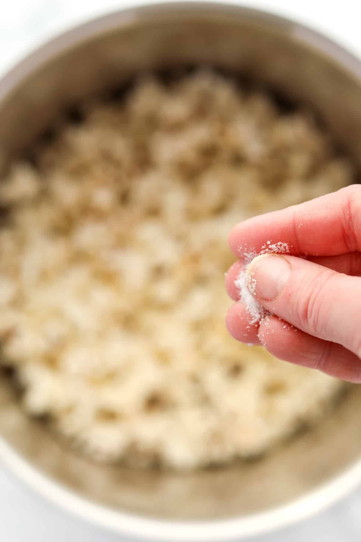Sprinkling fine salt into a large pot of homemade popcorn.
